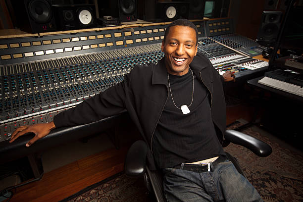 A young twentysomething African-American recording engineer in front of a mixing board in the studio