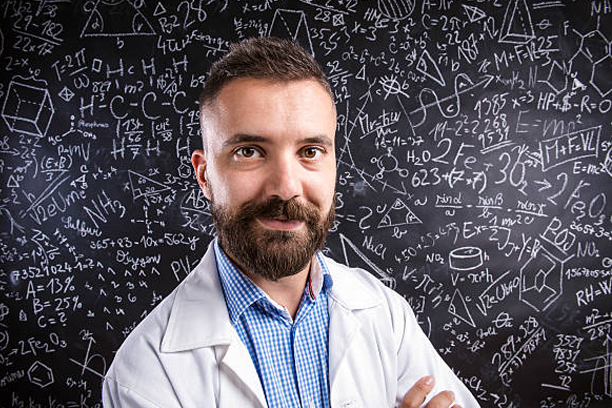 Close up of hipster teacher in white coat standing against big blackboard with mathematical symbols and formulas. Studio shot on black background.