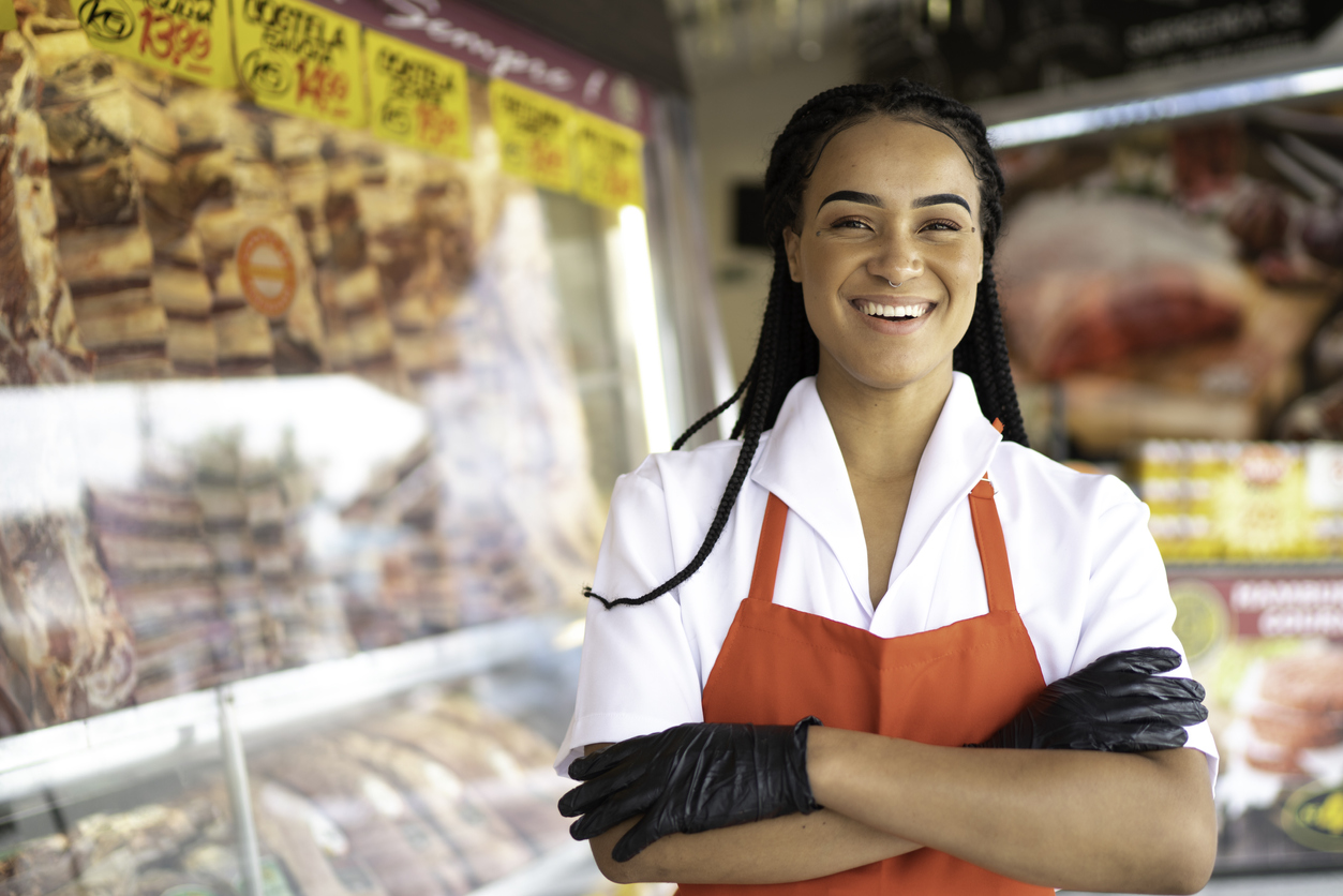 Portrait of a female butcher standing with arms crossed in front of a butchers shop