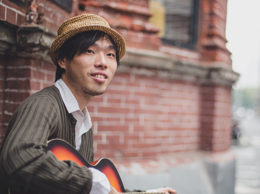 One man, standing on sthe street, playing acoustic guitar.