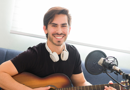 Portrait of a latin happy musician holding an acoustic guitar before singing and recording a song at home