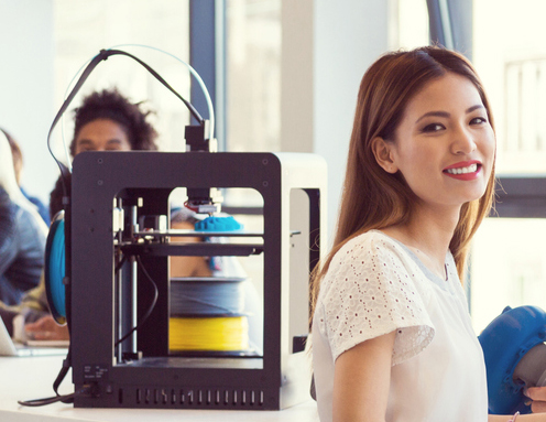 Start-up Business. Three young people sitting a the table, holding 3D printouts in hands and smiling at camera. 3D printer next to them.