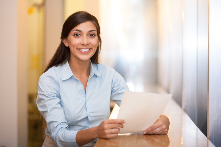 Closeup portrait of smiling at camera pretty adult Indian woman sitting at table in cafe and holding document